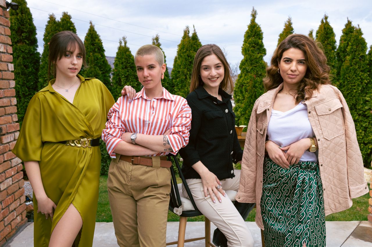 Four fashionable women smiling and posing confidently in a garden setting.